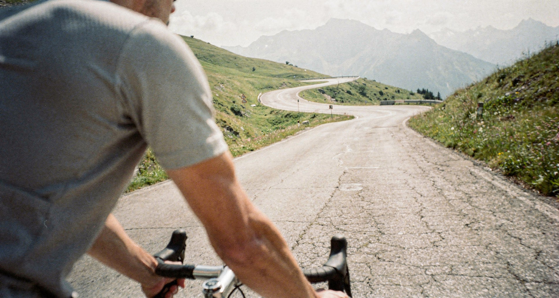 Blick über die Schulter eines Rennradfahrers auf eine sonnige Alpenpassstraße im Sommer