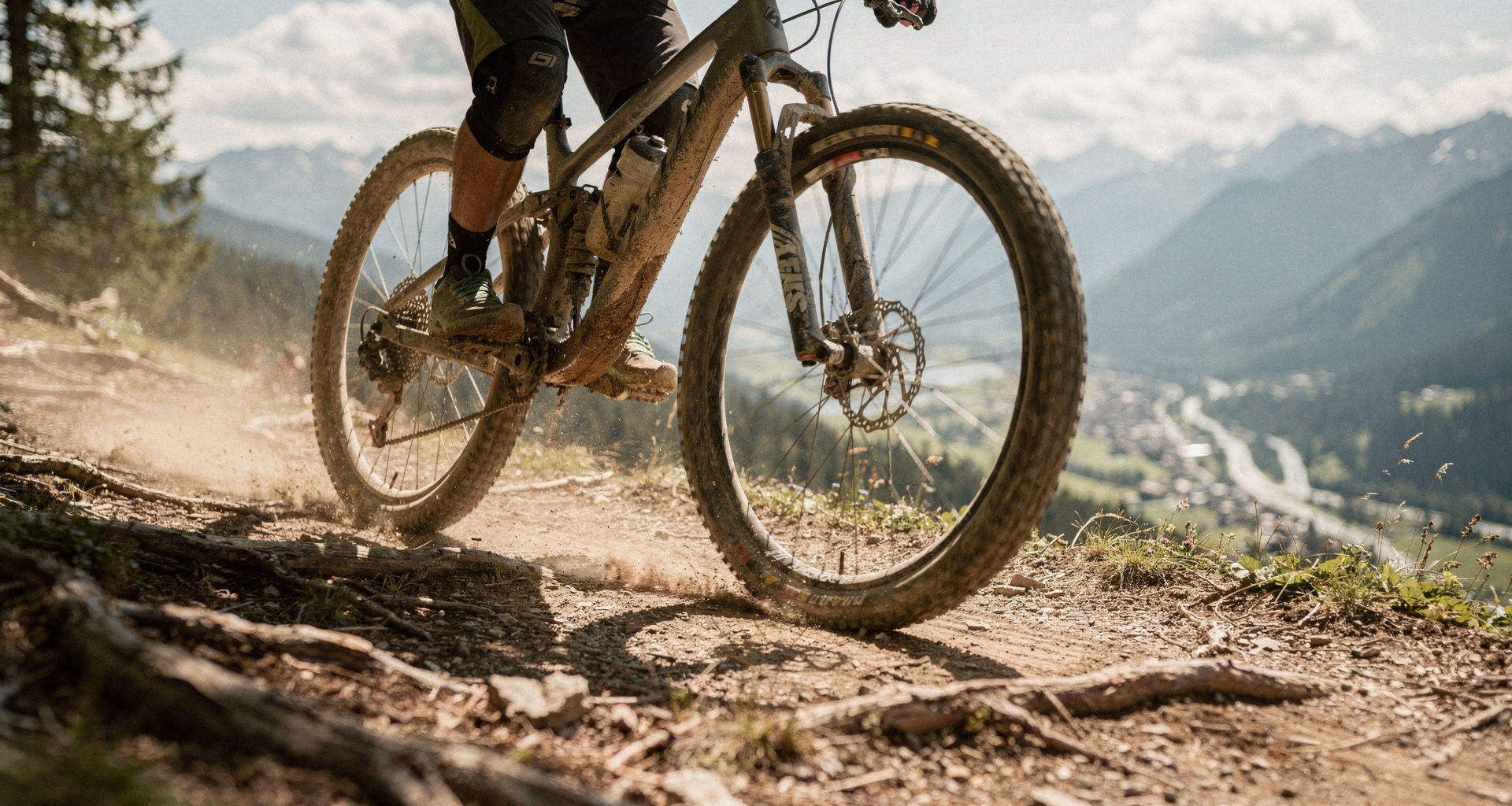 Mountainbike-Reifen und Beine des Fahrers auf einem staubigen Trail über einem Alpental