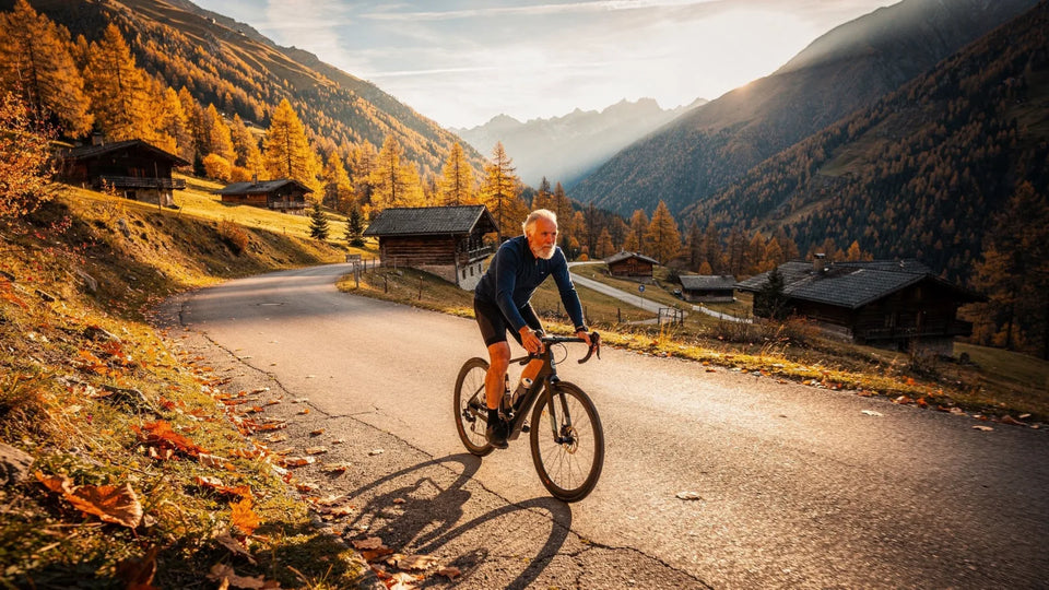Radfahrer um die 60 auf einer Talstraße an Chalets, im Herbst, im Licht der tiefen Abendsonne