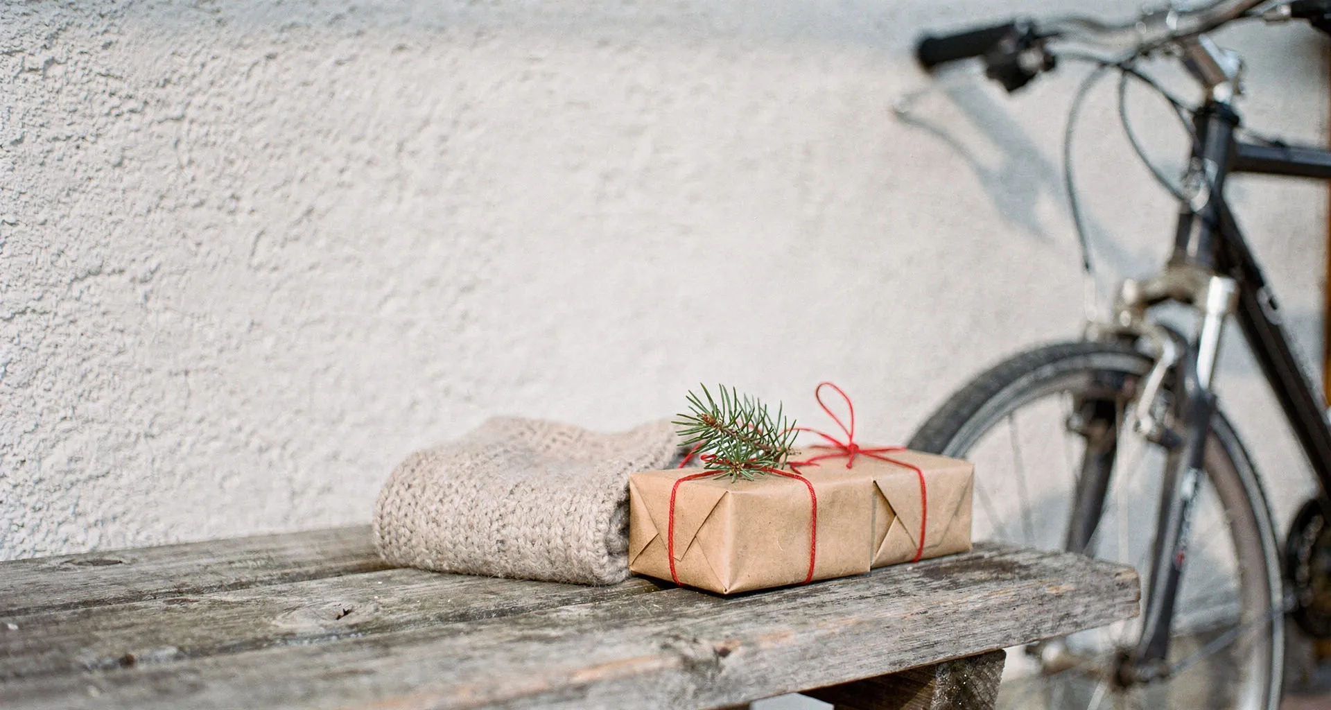 Geschenke für Radfahrer – verpackte Päckchen und Schal auf einer Holzbank, dahinter ein Fahrrad